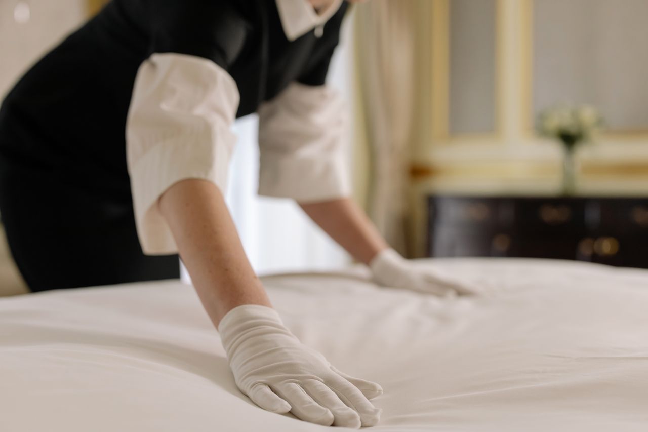 about-02 A housekeeper straightening the bed linens in a well-appointed hotel room.